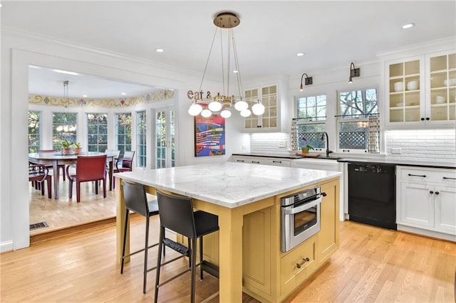 kitchen with a center island, stainless steel oven, light stone countertops, black dishwasher, and white cabinetry