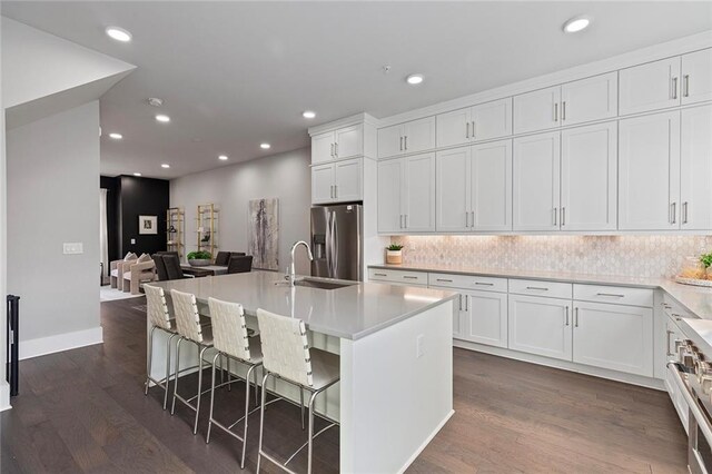 kitchen with dark hardwood / wood-style flooring, stainless steel fridge, an island with sink, a kitchen bar, and white cabinets