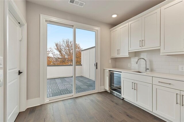 interior space featuring backsplash, dark wood-type flooring, sink, wine cooler, and white cabinetry