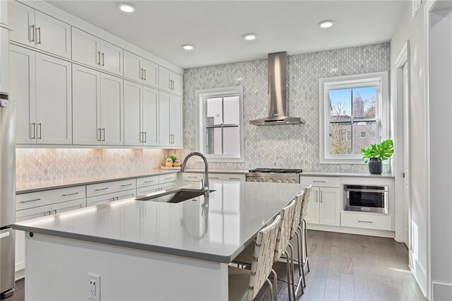 kitchen featuring sink, wall chimney exhaust hood, dark wood-type flooring, an island with sink, and white cabinets