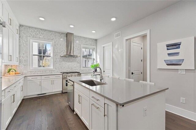 kitchen featuring sink, white cabinetry, wall chimney exhaust hood, and an island with sink