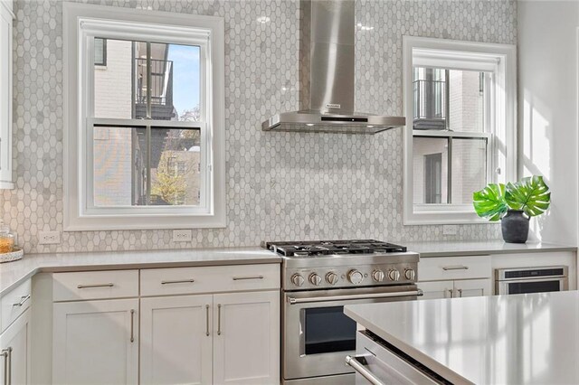 kitchen with appliances with stainless steel finishes, backsplash, white cabinetry, and wall chimney range hood