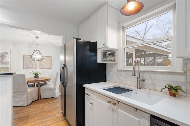 kitchen with sink, stainless steel fridge, white cabinets, backsplash, and hanging light fixtures