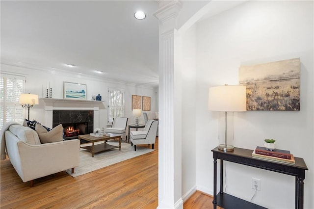 living room with a tiled fireplace, wood-type flooring, ornamental molding, and decorative columns