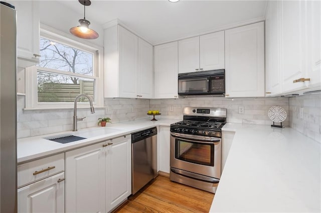 kitchen featuring sink, white cabinetry, hanging light fixtures, light hardwood / wood-style flooring, and stainless steel appliances