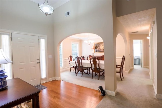 foyer entrance featuring arched walkways, light wood-type flooring, a towering ceiling, baseboards, and visible vents