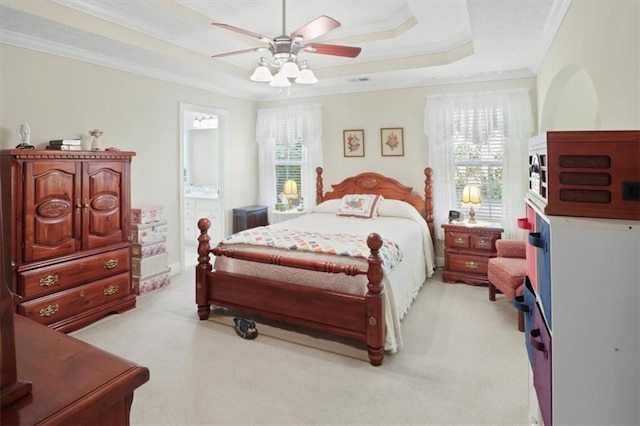 bedroom featuring light carpet, ensuite bath, a tray ceiling, and crown molding
