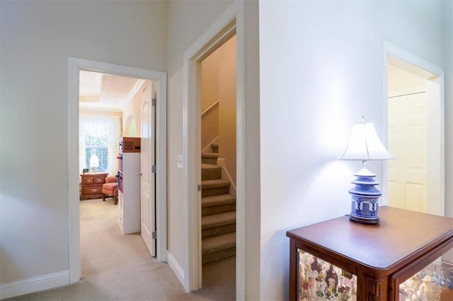 hallway with baseboards, stairs, and light colored carpet