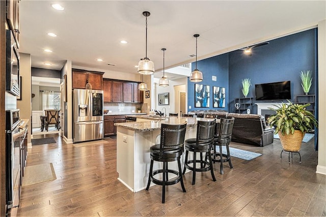 kitchen featuring a breakfast bar area, hanging light fixtures, appliances with stainless steel finishes, dark hardwood / wood-style flooring, and light stone countertops