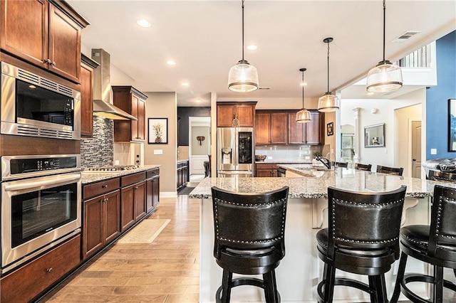 kitchen with a breakfast bar, sink, hanging light fixtures, appliances with stainless steel finishes, and wall chimney range hood