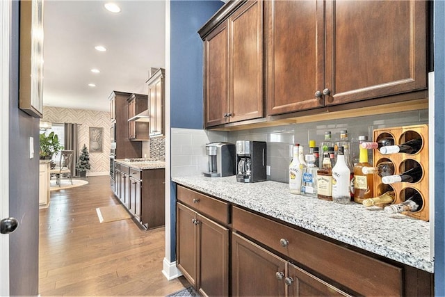 kitchen with decorative backsplash, stainless steel oven, light hardwood / wood-style floors, cooktop, and light stone countertops