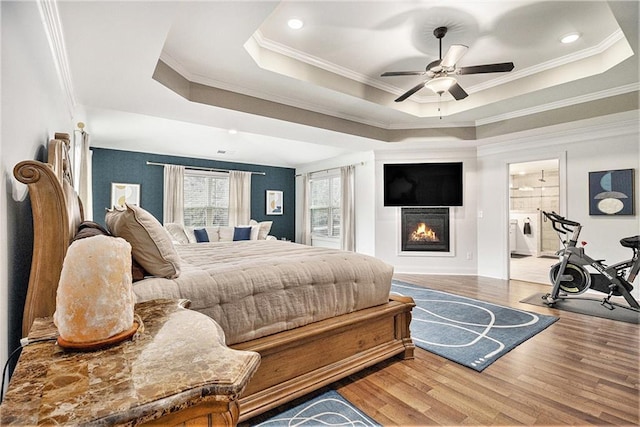 bedroom featuring crown molding, a tray ceiling, wood-type flooring, and ensuite bath