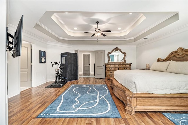 bedroom featuring ceiling fan, ornamental molding, a tray ceiling, and hardwood / wood-style floors