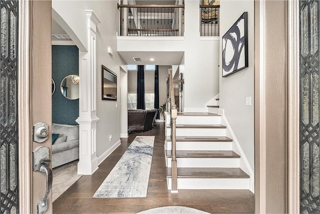 foyer entrance featuring dark hardwood / wood-style flooring, decorative columns, and a high ceiling