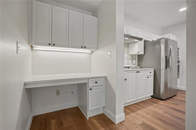 kitchen with white cabinets, light wood-type flooring, built in desk, and stainless steel appliances