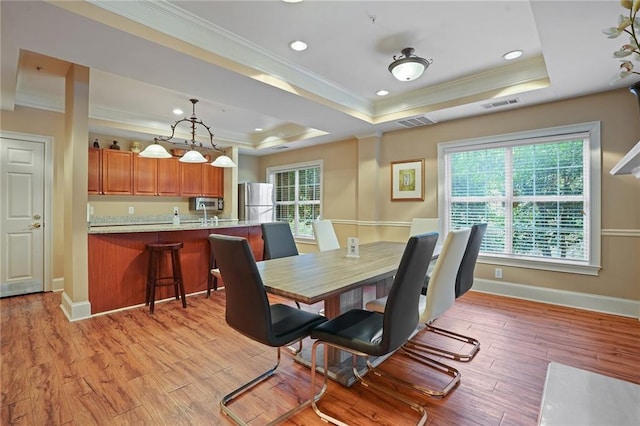 dining room with a tray ceiling, light hardwood / wood-style flooring, and crown molding