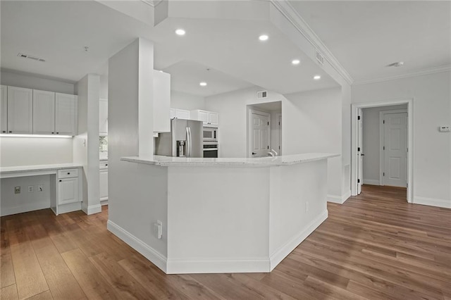 kitchen featuring appliances with stainless steel finishes, built in desk, white cabinetry, and hardwood / wood-style floors