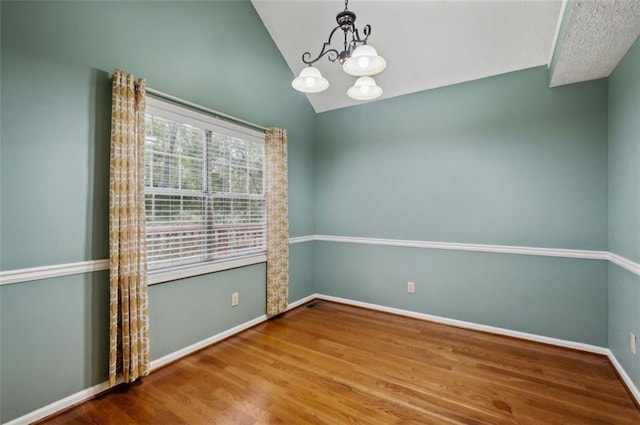 empty room with wood-type flooring, an inviting chandelier, and lofted ceiling