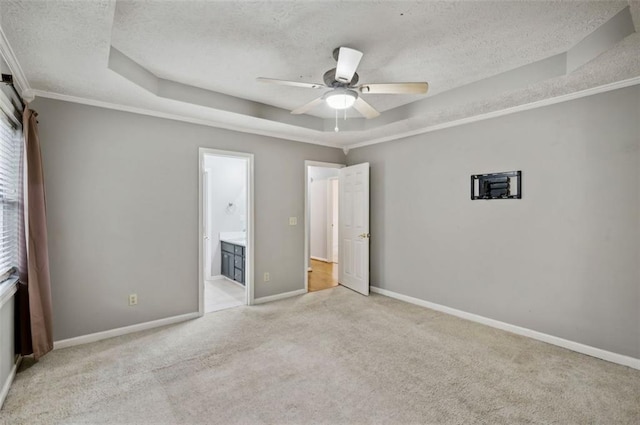 unfurnished bedroom with a tray ceiling, ensuite bath, ceiling fan, and light colored carpet