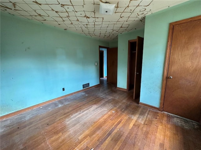 spare room with wood-type flooring, visible vents, and baseboards