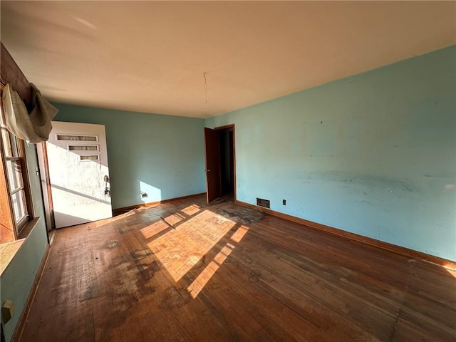 unfurnished room featuring wood-type flooring, visible vents, and baseboards