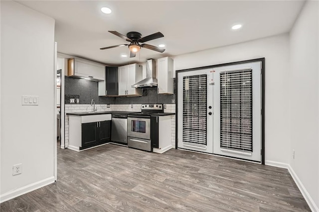 kitchen with appliances with stainless steel finishes, wall chimney exhaust hood, wood-type flooring, tasteful backsplash, and ceiling fan