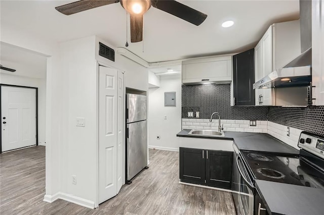 kitchen featuring appliances with stainless steel finishes, white cabinets, wall chimney range hood, light hardwood / wood-style flooring, and sink