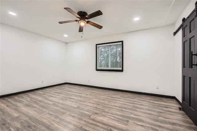 spare room with ceiling fan, a barn door, and light wood-type flooring