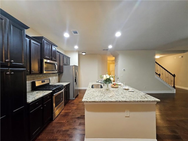 kitchen featuring sink, decorative backsplash, a kitchen island with sink, stainless steel appliances, and light stone countertops