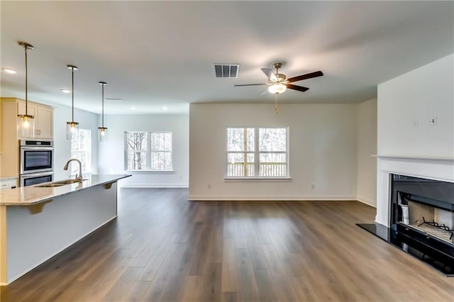 unfurnished living room featuring a sink, a fireplace with raised hearth, a ceiling fan, visible vents, and dark wood-style floors