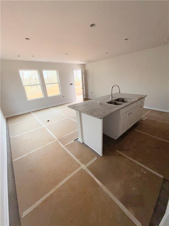 kitchen featuring light stone countertops, baseboards, a center island with sink, white cabinets, and a sink