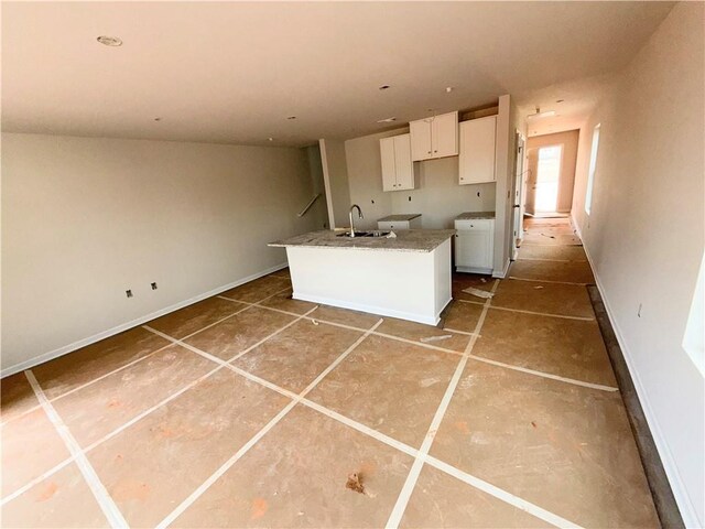 kitchen featuring white cabinets, a sink, tile patterned flooring, baseboards, and a center island with sink