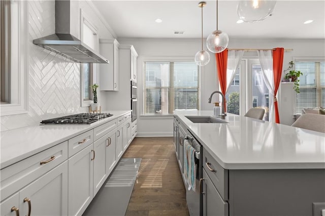 kitchen featuring pendant lighting, sink, stainless steel appliances, an island with sink, and wall chimney exhaust hood