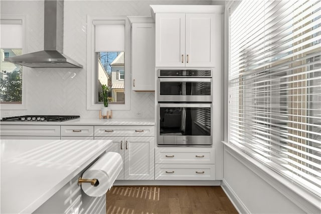 kitchen with appliances with stainless steel finishes, backsplash, dark hardwood / wood-style floors, white cabinets, and wall chimney exhaust hood