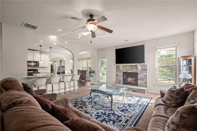 carpeted living room with ceiling fan and a stone fireplace