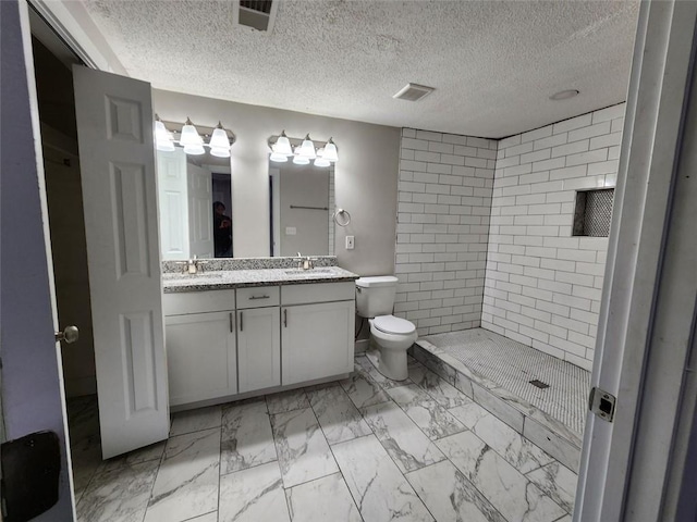 bathroom with toilet, vanity, a textured ceiling, and tiled shower