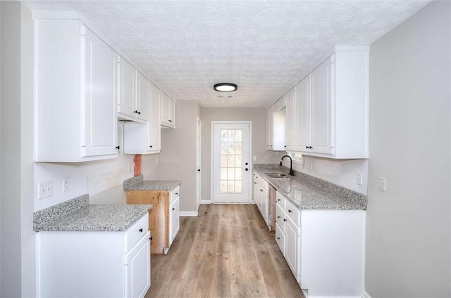 kitchen with white cabinetry, light hardwood / wood-style floors, sink, and a textured ceiling