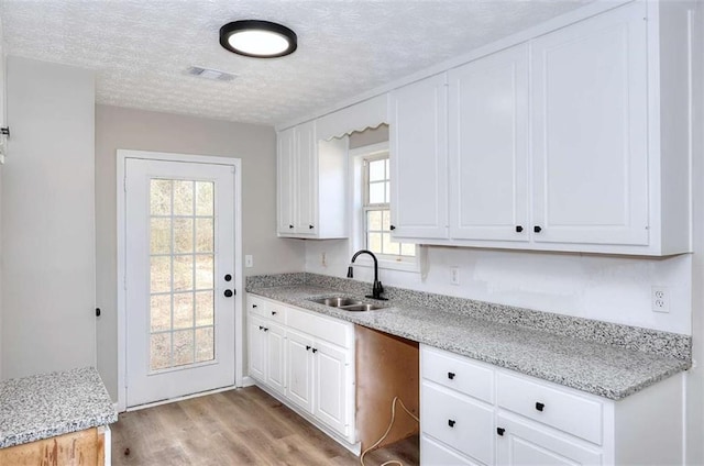 kitchen featuring sink, light hardwood / wood-style flooring, a textured ceiling, light stone countertops, and white cabinets