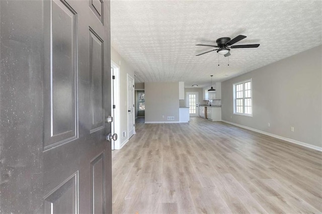 unfurnished living room featuring ceiling fan, light hardwood / wood-style flooring, and a textured ceiling