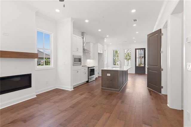 kitchen featuring wall chimney range hood, white cabinets, a center island with sink, and stainless steel appliances