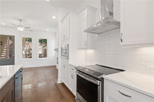 kitchen featuring wall chimney range hood, decorative backsplash, light stone countertops, stainless steel appliances, and white cabinets