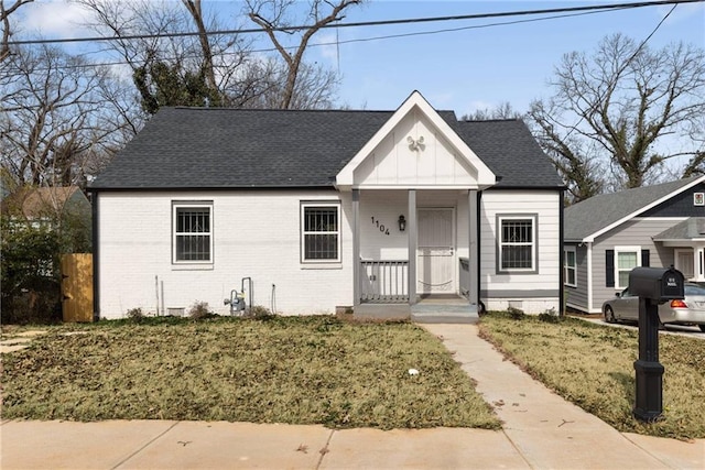 bungalow-style home with brick siding, roof with shingles, a front lawn, and board and batten siding