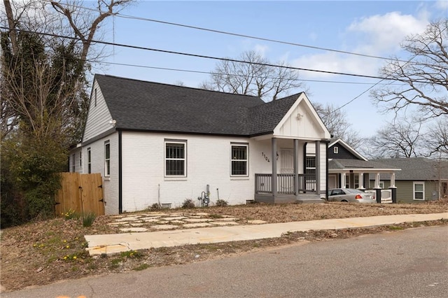 view of front facade with covered porch, roof with shingles, a gate, and brick siding