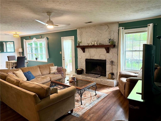 living area featuring a textured ceiling, wood finished floors, ceiling fan, a stone fireplace, and ornamental molding