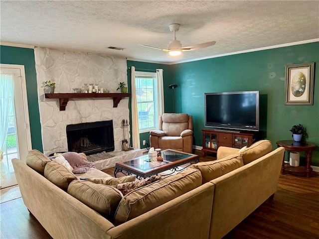 living room with wood finished floors, a textured ceiling, crown molding, a fireplace, and ceiling fan