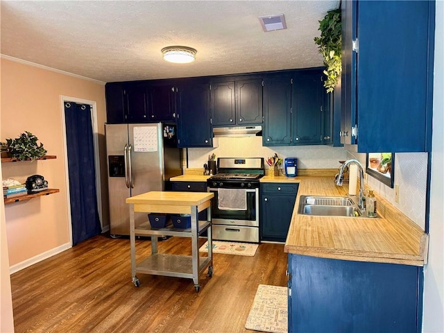kitchen with appliances with stainless steel finishes, a sink, under cabinet range hood, light countertops, and dark wood-type flooring