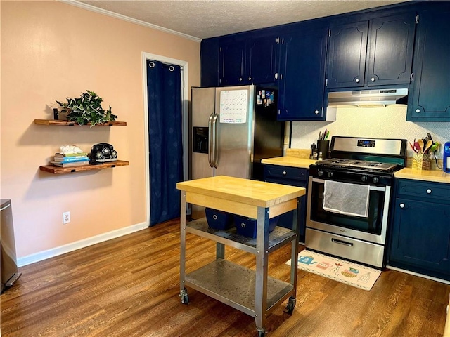 kitchen with stainless steel range with gas stovetop, under cabinet range hood, blue cabinetry, dark wood-type flooring, and crown molding