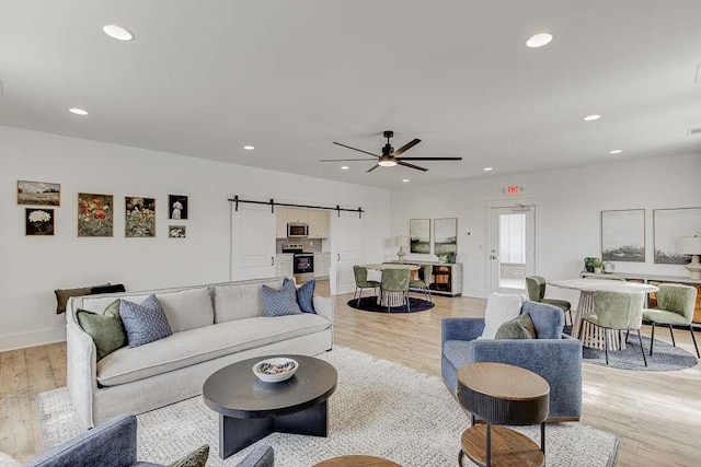 living room featuring a barn door, ceiling fan, and light hardwood / wood-style flooring