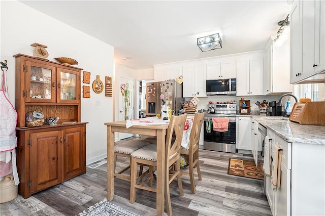 kitchen with sink, white cabinetry, light stone counters, wood-type flooring, and stainless steel appliances