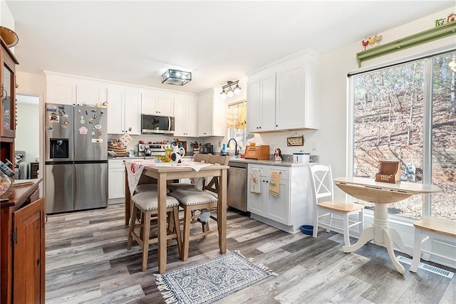 kitchen with stainless steel appliances, sink, white cabinets, and light hardwood / wood-style floors